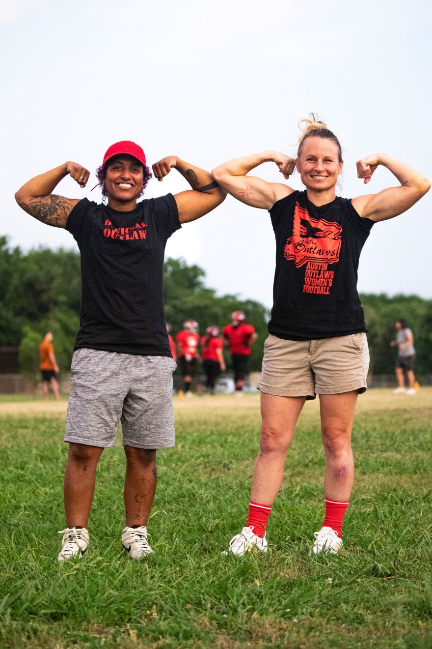 Two people standing in a field are smiling and showing their biceps in front of the camera