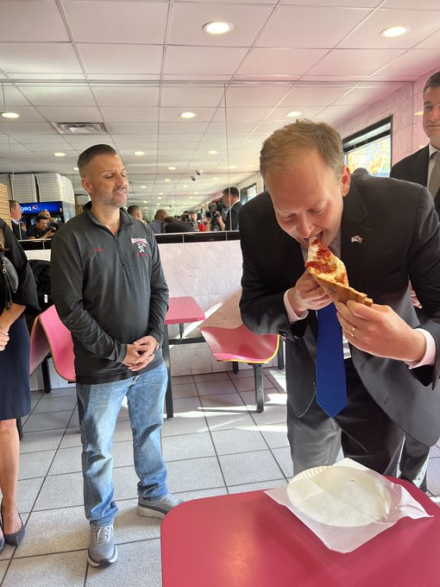 Long Island Representative Lee Zeldin, the Republican candidate for New York governor, takes a bite of the chicken parm pizza at Paesan's Pizza, his favorite when he was a student at the State University of New York at Albany. Owner Frank Scavio is on the left.