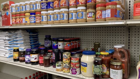 Shelves at The House of Peace food pantry containing peanut butter, syrup and other condiments.
