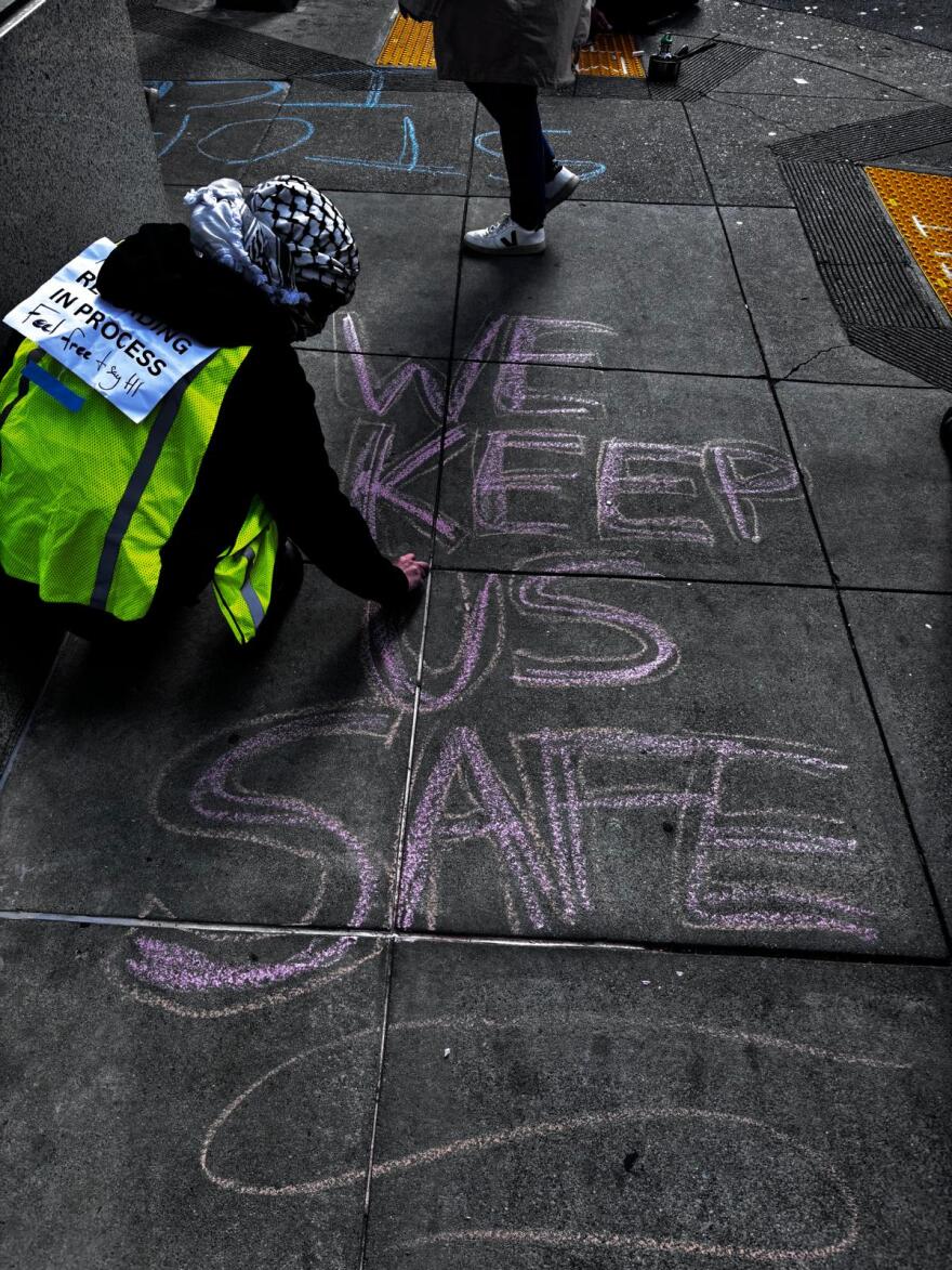 Crouched, Alice draws large letters on the sidewalk with chalk.