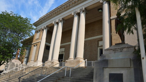 The front of a brown brick and stone building with columns, stairs and statues of soldiers.