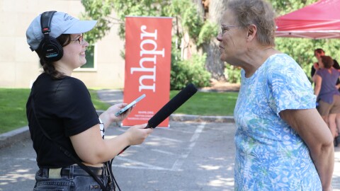 A young woman on the left has a recording kit and mic which she holds up for an older woman on the right to speak into. They are both smiling. 