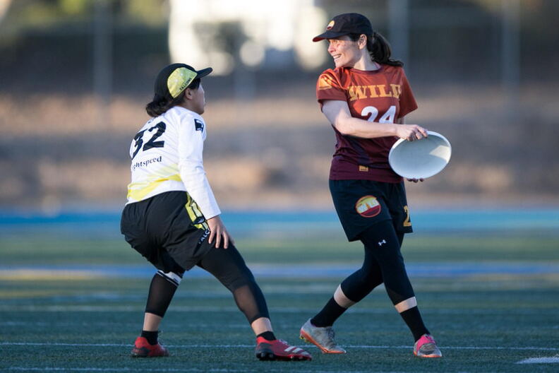 Two ultimate frisbee players face each other on a sports field in front of a blurred background. Player number 24 holds a frisbee.