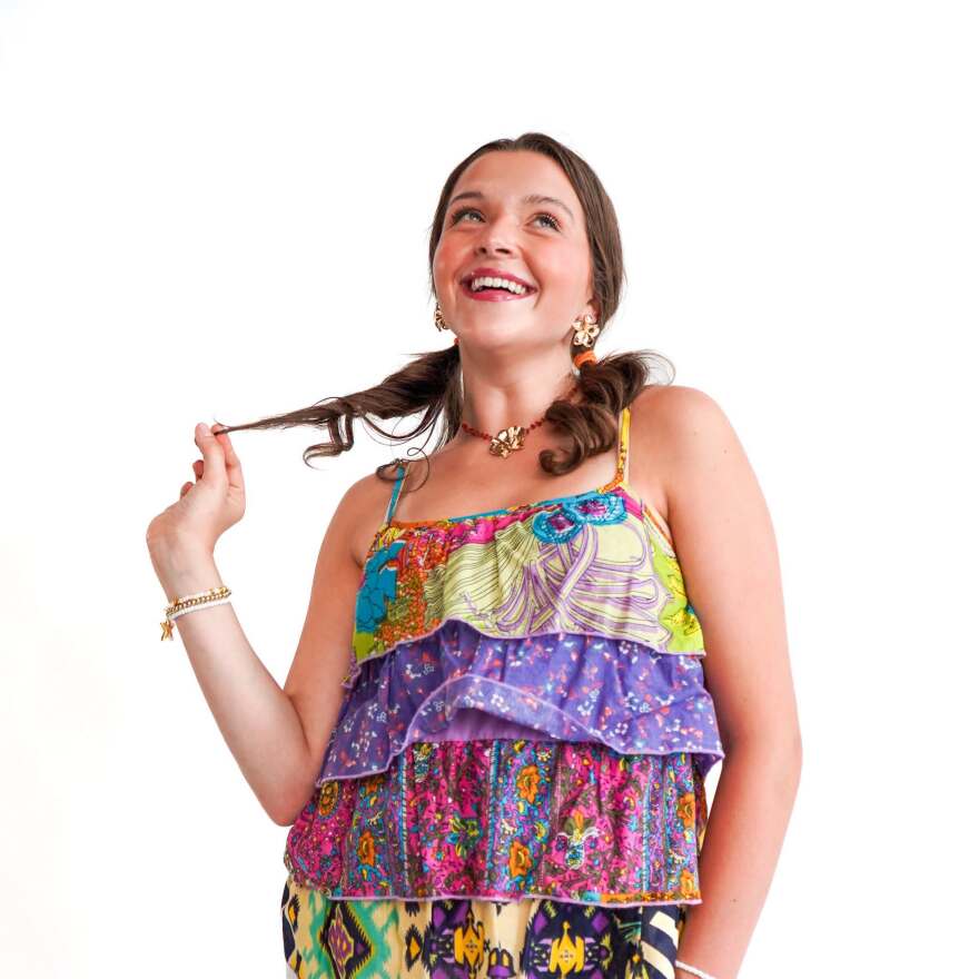 A young woman wearing colorful clothing, smiling, twisting her hair