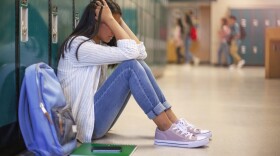 A frustrated teenager sits against the lockers in a school hallway. (Getty Images)