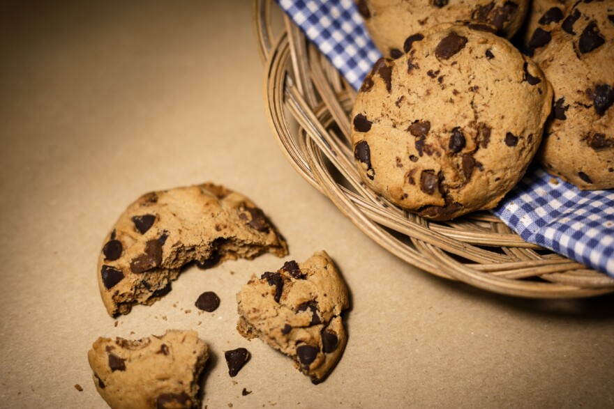 Chocolate chip cookies in a basket and a broken cookie nearby.