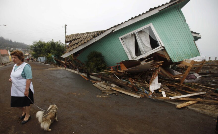 Following one of the largest earthquakes ever recorded, a woman stands in front of a destroyed home in Pelluhue.