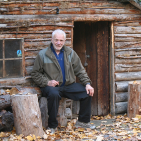 Legendary Alaska adventurer Dick Griffith sits in front of a log cabin in Chugach State Park. Griffith passed away Tuesday, Dec. 2, 2025.
