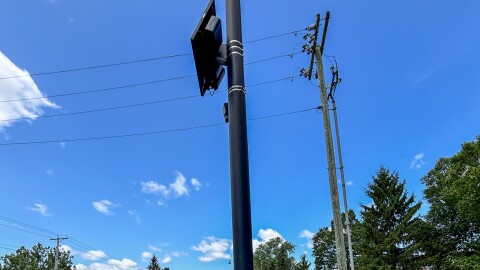 A sign of protest saying "Who watches the Watchers" sits under a Flock camera in the 2200 block of St. Joe Center Road.