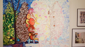 An unfinished painting hangs on a white wall. The finished portion is on the left, with abstracted green and brown trees leading into a half-done tree in fall colors. the remainder is sketched out in graphite and colored pencils.