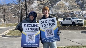 Two volunteers for the Brave Utahns Rapid Response Network pose holding signs that read "Decline to Sign. I am unpaid. I am a Utah resident. I care about your voting rights."