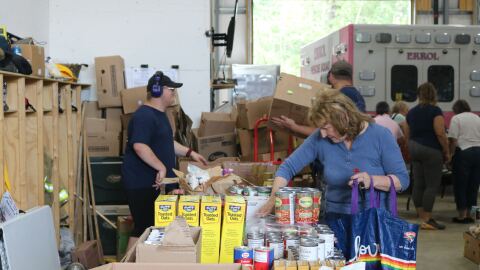A person picks out something from a line of cans on a table at a food pantry.