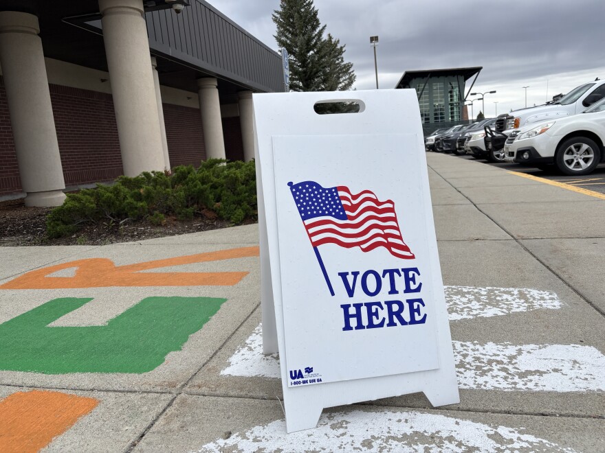 A white sandwich-style poster says "VOTE HERE" with an image of an American flag.