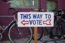 A sign says "This Way To Vote" with bicycles behind it