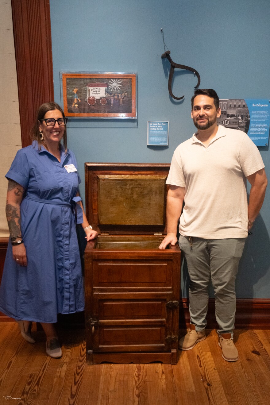 Two people stand beside an old fashioned wooden ice box