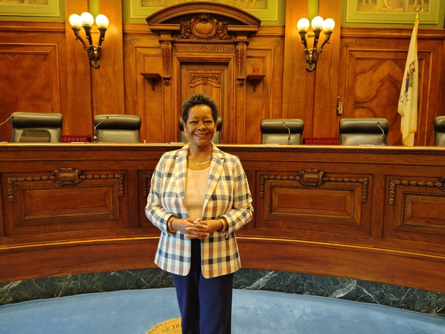 A woman in a plaid blazer stands smiling in front of a judges' bench.