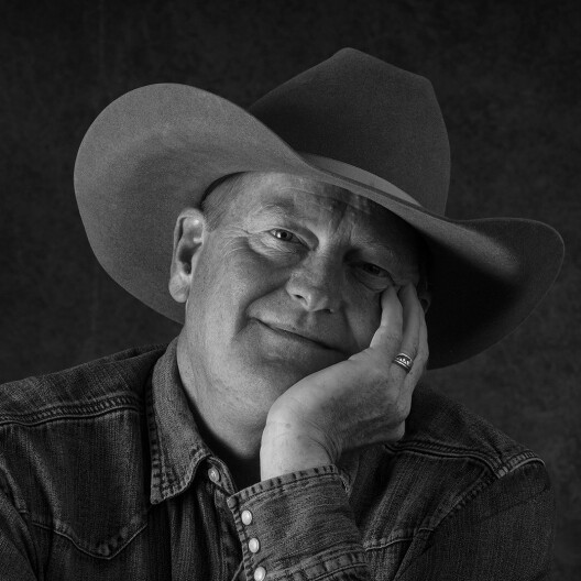  Author Craig Johnson sits with his head in his hand smiling. 