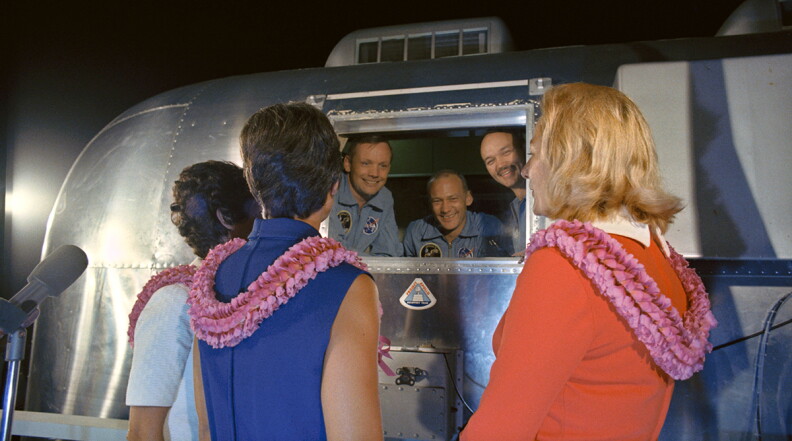 The Apollo 11 crewmen, still under a 21-day quarantine, are greeted by their wives.