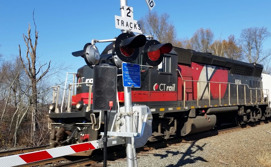 A CTrail passenger train races by a rail crossing in Longmeadow, Massachusetts