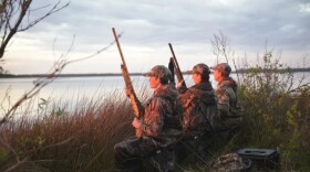 Three people in camo with rifles outside