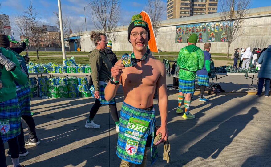 shirtless man holds up badge and smiles.
