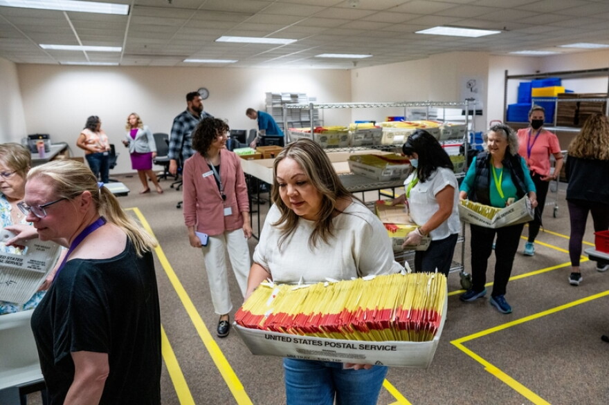 Workers handling U.S. Postal Service trays full of ballots.