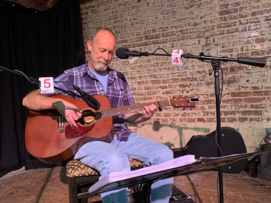 Gray playing his guitar in front of a mic.