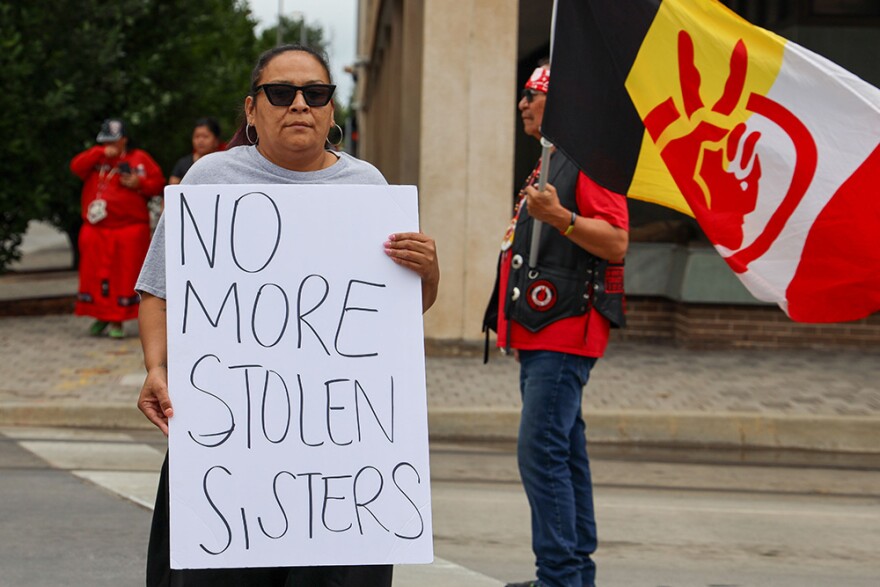 Paula Goodbear (Cheyenne and Arapaho) holds a sign saying ‘No More Stolen Sisters’ while Toma Hubert Stands (Lakota), holding an American Indian Movement flag, helps her cross an Oklahoma City intersection during an MMIP Honor Walk on May 5, 2024.