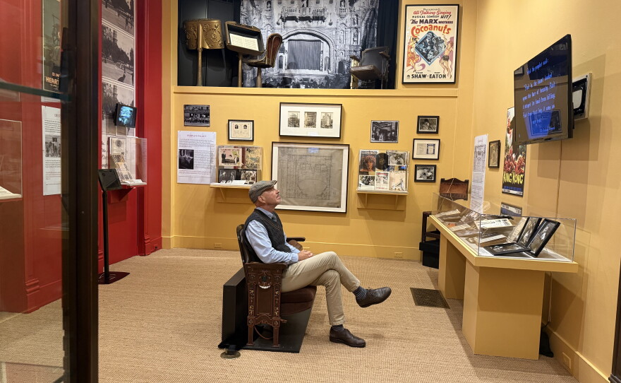 A man sits in a reproduced theatre seat in the middle of an exhibit on the early history of cinema at the Henry B. Plant Museum. 