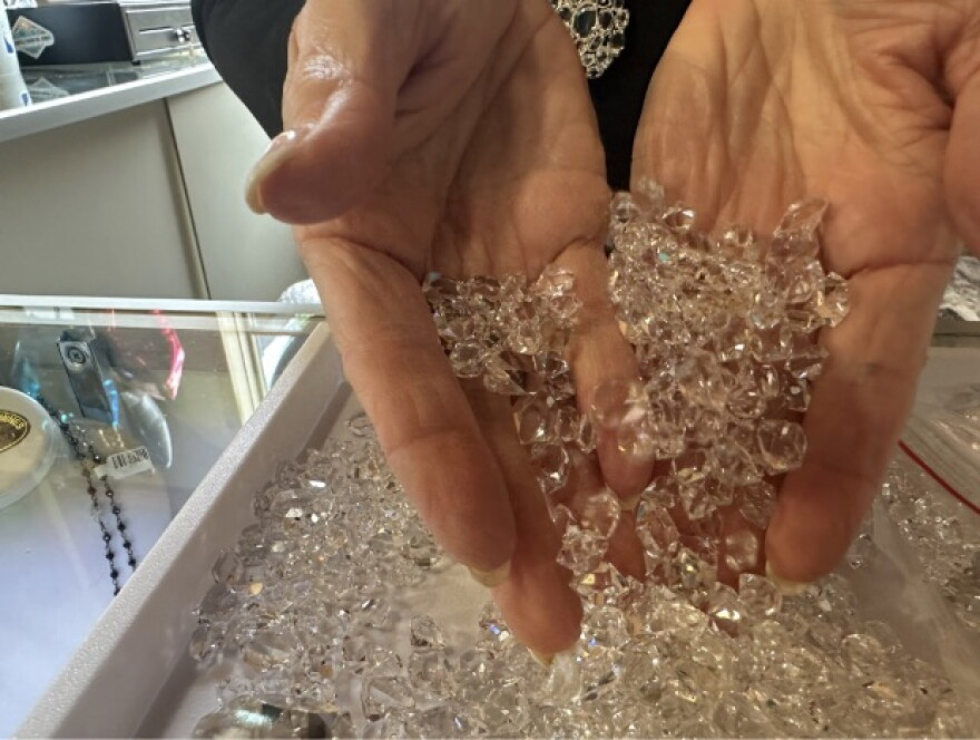 A woman's hand scoops up a tray full of diamond looking stones that are actually Herkimer Diamond quartz.