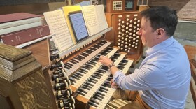 St. Paul's Episcopal Church Director of Music Jon Gilbin plays the massive pipe organ at St. Paul's. A man in a blue button up and khakis performs on a massive, four-keyboard organ. He reads music from an iPad.