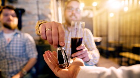 Drunk man with a beer in hand giving car key to the sober friend while enjoying in the bar.