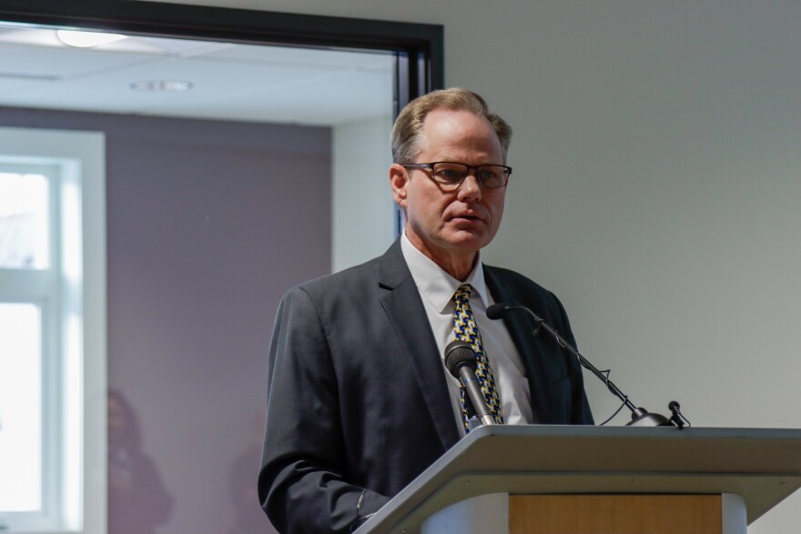 A man in a suit and glasses speaks behind a podium.