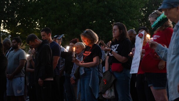 People stand in a group holding candles in the evening. 