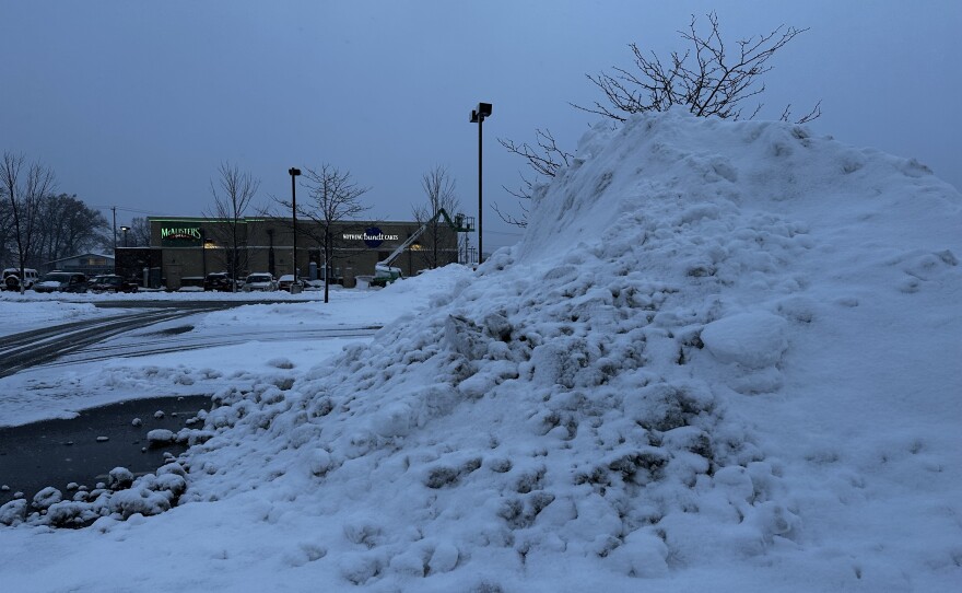 Snow piles more than 10 feet high fill a shopping center parking lot in Elkhart after the weekend storm, as crews work to clear heavy, wet snow from the area.