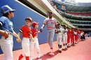 a man in a baseball uniform holds hands with a line of children also in baseball uniforms