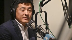A man inside a radio studio sits at a microphone talking.