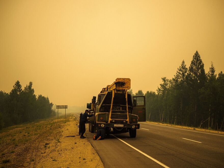 Men repair their truck in smoke from a forest fire on a road near Magaras, in the republic of Sakha, Siberia, in July. [Dimitar Dilkoff / AFP via Getty Images]