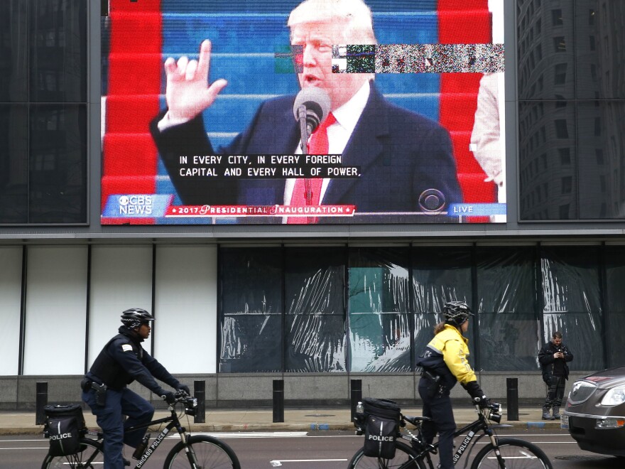 Chicago police officials ride bikes by a broadcast of President Trump's inaugural address on Jan. 20. The president has threatened to "send in the Feds" to intervene in the city's law enforcement.