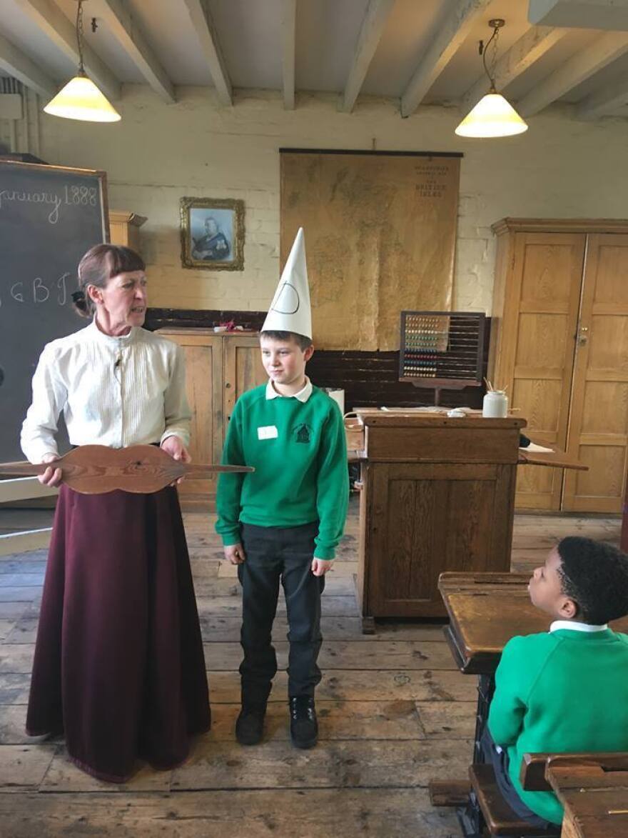 Miss Perkins chastises a visiting student with a dunce cap.