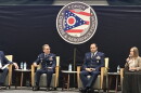 Three men and a woman sit in chairs on a stage below an an Ohio Defense & Aerospace Forum sign.
