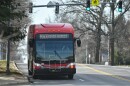 A red commuter bus moves on a quiet city street. It has a lighted sign on it that reads "MAX River Market."