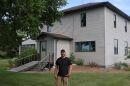 A man in his forties wearing a black shirt stands in front of his home, which has stood for over a hundred years.