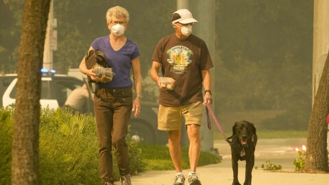 An older couple wearing N-95 masks walks their black lab dog as smoke from a wildfire fills the air.