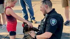 A police officer holds a K-9 helper as a young girl pets the dog.