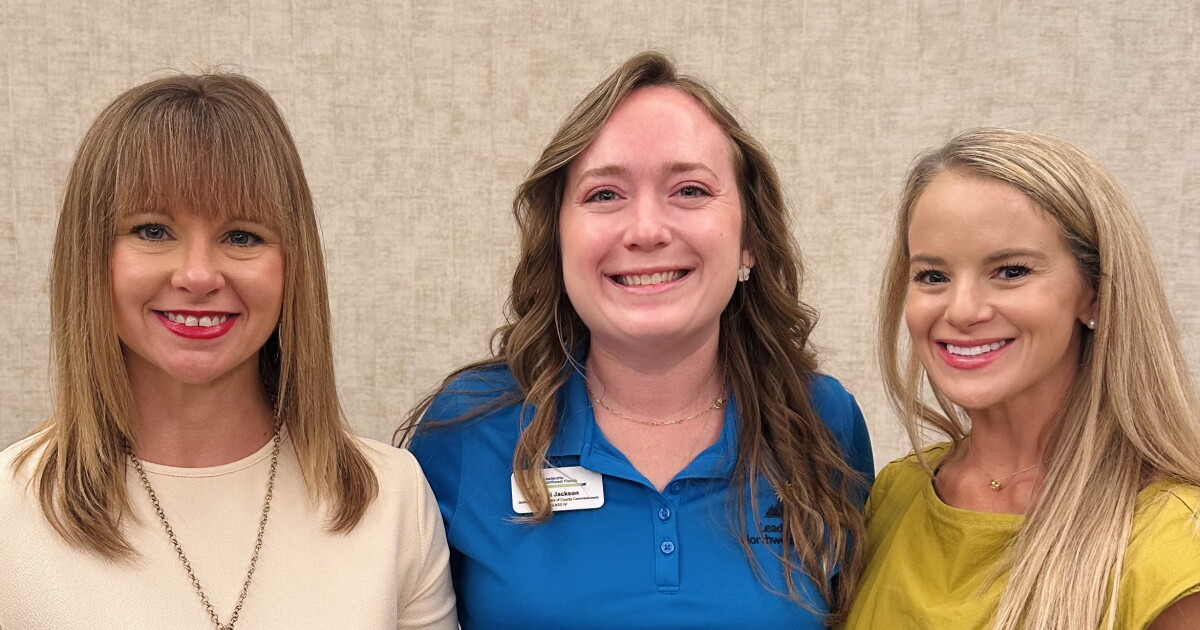 Three women in business casual attire pose with a plaque highlighting Leadership Northwest Florida Legacy for Kelsi Jackson in the middle.