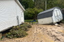 A storage shed that has been knocked over by flood waters sits in a muddy yard.