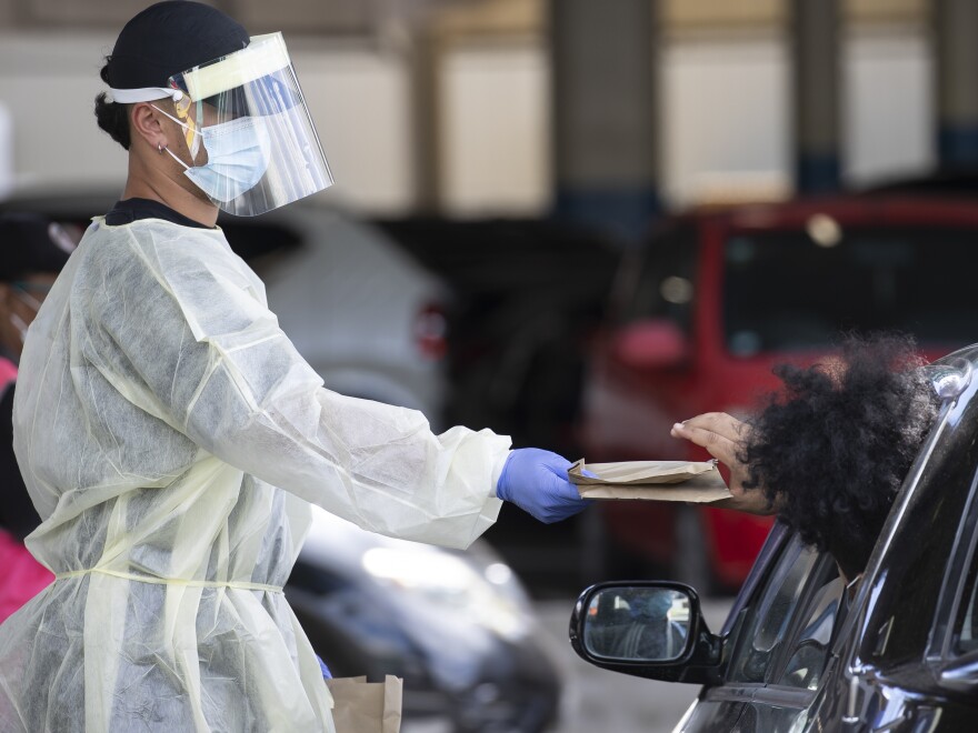 A health worker gives out Rapid COVID-19 antigen self-test kits at the Waipareira Trust drive-in COVID-19 testing station in Auckland, New Zealand, Tuesday, March 8, 2022. Back in August, 2021, New Zealand's government put the entire nation into lockdown after a single community case of the coronavirus was detected. On Tuesday, when new daily cases hit a record of nearly 24,000, officials told healthcare workers they could go back to work in understaffed COVID-19 wards even if they were mildly sick themselves. (Brett Phibbs/New Zealand Herald via AP)