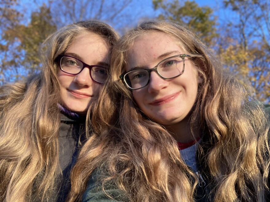 Two girls with long hair and glasses pose for a photo.