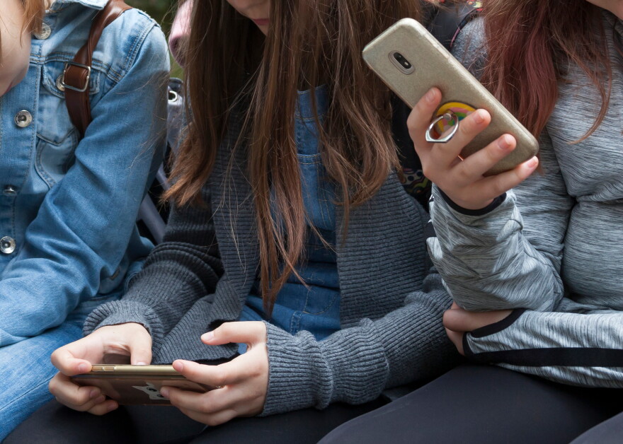 Two young teenage girls sitting holding smartphones in their hands.